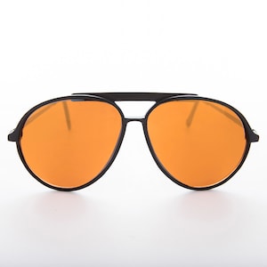 K&ouml;nnte beinhalten: Schwarze Aviator-Sonnenbrille mit orangenen Gl&auml;sern. Die Sonnenbrille hat einen Metallrahmen und eine Doppelbr&uuml;cke.