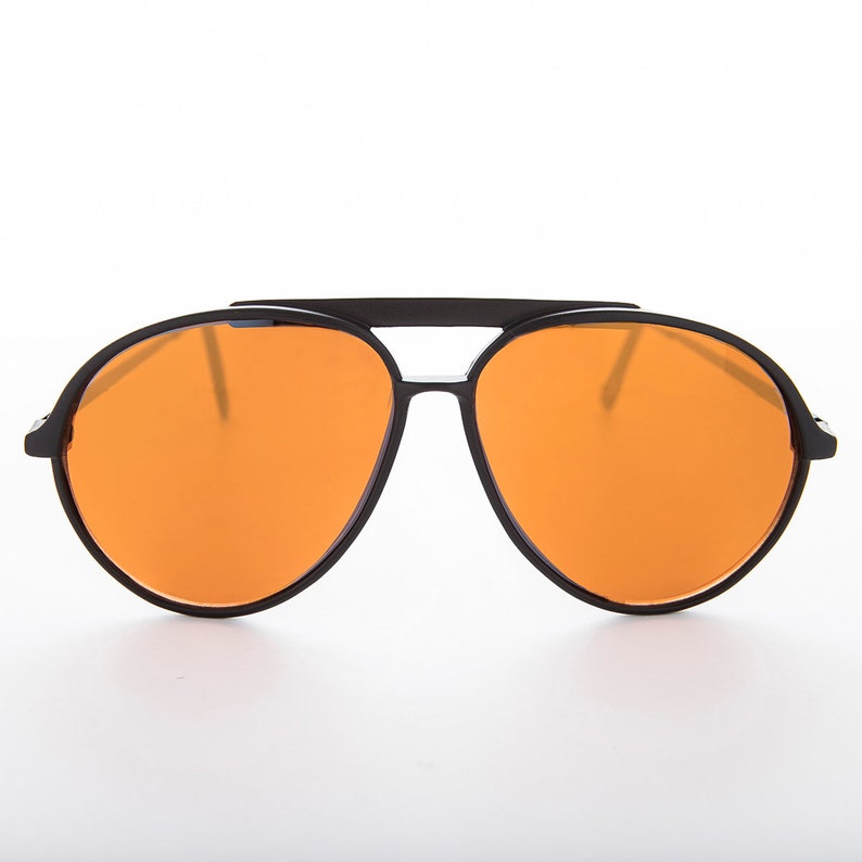K&ouml;nnte beinhalten: Schwarze Aviator-Sonnenbrille mit orangenen Gl&auml;sern. Die Sonnenbrille hat einen Metallrahmen und eine Doppelbr&uuml;cke.