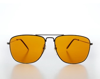 May include: Black-framed sunglasses with orange-tinted lenses. The sunglasses have a classic aviator design with a double bridge and a sleek, modern aesthetic. The lenses are a vibrant orange color.