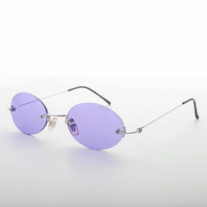 May include: Oval-shaped sunglasses with purple lenses and a silver metal frame. The temples are thin and silver, with black tips. The lenses are a solid, light purple color.