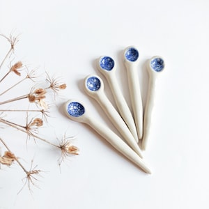 Könnte beinhalten: Fünf weiße Keramikslöffel mit blau-weiß gesprenkelten Designs auf der Schale jedes Löffels.