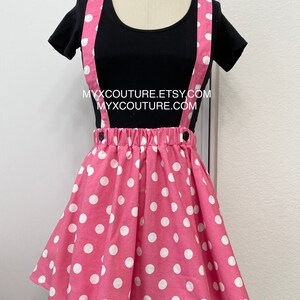 Puede incluir: Una camiseta negra con cuello redondo combinada con una falda rosa de lunares y tirantes. La falda tiene cintura fruncida y est&aacute; adornada con grandes lunares blancos. Los tirantes son rosas con lunares blancos. El texto "MYXCOUTURE.ETSY.COM" y "MYXCOUTURE.COM" es visible.