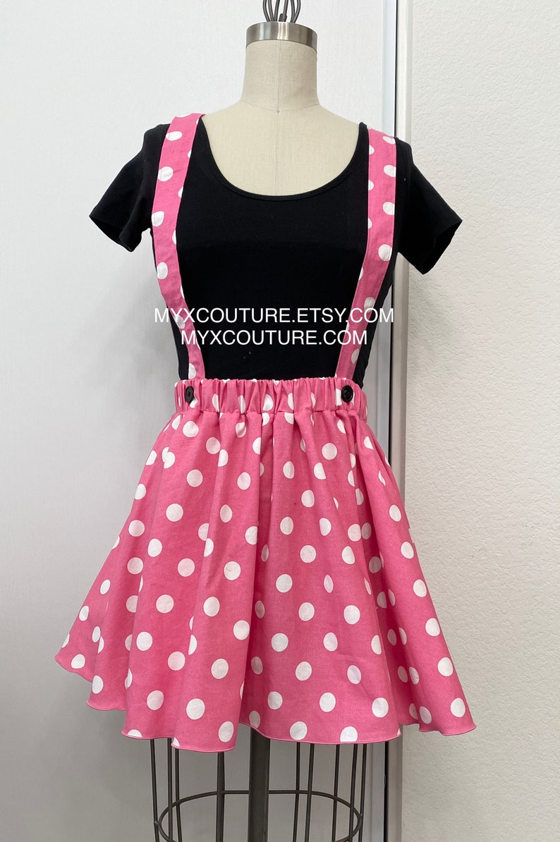 Puede incluir: Una camiseta negra con cuello redondo combinada con una falda rosa de lunares y tirantes. La falda tiene cintura fruncida y est&aacute; adornada con grandes lunares blancos. Los tirantes son rosas con lunares blancos. El texto "MYXCOUTURE.ETSY.COM" y "MYXCOUTURE.COM" es visible.