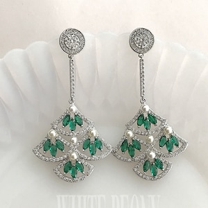 May include: A pair of silver dangle earrings with a green and white design. The earrings feature a circular top with clear stones, a long silver chain, and a three-tiered design with green stones and white pearls.
