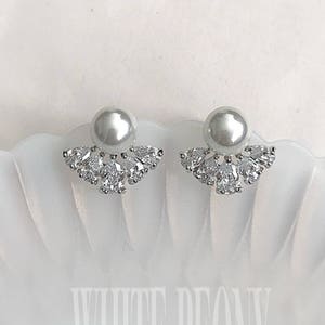 May include: A pair of silver earrings with a pearl and clear crystal accents. The earrings are on a white background.