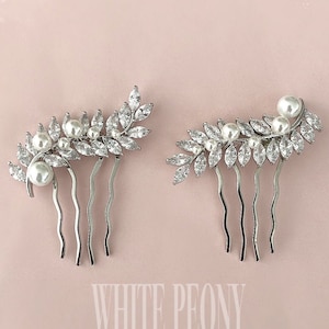 May include: Two silver hair combs featuring a leaf and pearl design. The combs are adorned with small, clear rhinestones and white pearls.