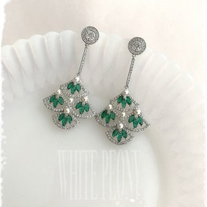 May include: A pair of silver dangle earrings with a Christmas tree design. The earrings are adorned with green and white crystals.