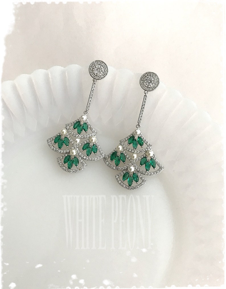 May include: A pair of silver dangle earrings with a Christmas tree design. The earrings are adorned with green and white crystals.