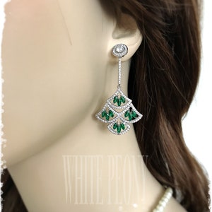 May include: Silver dangle earrings with a teardrop design. The earrings feature clear and green crystals.