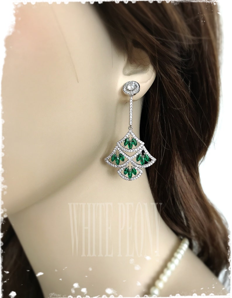 May include: Silver dangle earrings with a teardrop design. The earrings feature clear and green crystals.