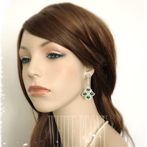 May include: A pair of silver dangle earrings with green and clear crystal accents. The earrings feature a cascading design with multiple tiers of crystals.