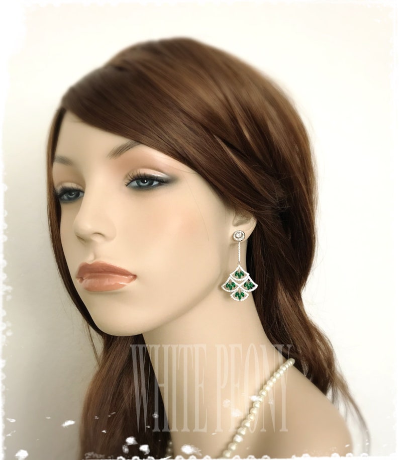 May include: A pair of silver dangle earrings with green and clear crystal accents. The earrings feature a cascading design with multiple tiers of crystals.