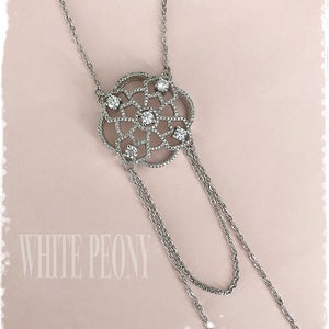 May include: A silver necklace with a delicate, circular pendant featuring a geometric design with small clear stones. The pendant hangs from two chains.