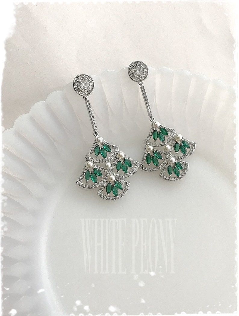 May include: A pair of silver dangle earrings with green and white stones. The earrings feature a fan-shaped design with multiple layers of stones.