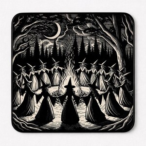 May include: A square mousepad featuring a black and white woodcut-style illustration of a group of figures in pointed hats and long robes holding hands in a circle around a large bonfire in a forest under a crescent moon and starry night sky.