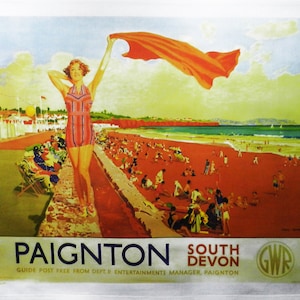 May include: A vintage-style beach scene illustration on a white background. A woman in a red and white striped swimsuit holds a red scarf on a beach with many people. The text "Paignton South Devon" is at the bottom.