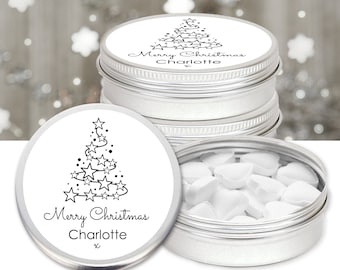 May include: Silver tin containers with lids featuring a black and white Christmas tree design made of stars. The text "Merry Christmas Charlotte" is printed on the lid. One tin is open, revealing heart-shaped candies.