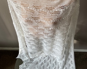 May include: White crochet shawl with a delicate lace pattern. The shawl is draped over a mannequin and has a scalloped edge.