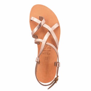 May include: Rose gold leather sandals with crisscross straps and an ankle strap with a buckle. The sandals have a light brown sole and the text "Iris Genuine Leather Greek Hand Made 37".