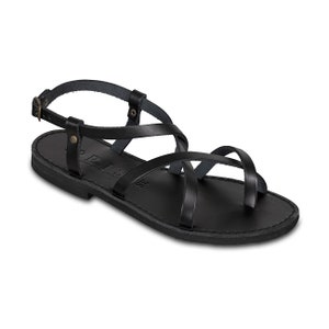 May include: Black leather sandals with multiple straps and a buckle closure. The sandals have a flat sole and a toe loop. The word "PRIS" is visible on the side of the sole. The sandals are a size 38.