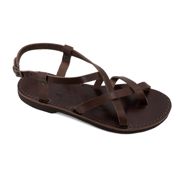 May include: Brown leather sandal with multiple straps crossing over the foot and ankle. The sandal has a simple design with a buckle closure and a flat sole. The sandal is a size 7.