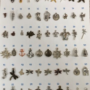 Pu&ograve; includere: Sessanta ciondoli in metallo assortiti con vari temi marini e da spiaggia, tra cui conchiglie, stelle marine, ancore, tartarughe e fari. I ciondoli sono disposti in file su uno sfondo bianco, numerati da 1 a 60.