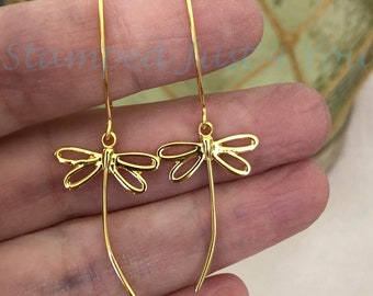 May include: Gold-toned dangle earrings featuring a dragonfly design. The earrings are made of thin wire and have a simple, elegant look.