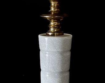 May include: A tall, elegant candle holder with a white, patterned candle. The base and accents are gold-toned metal, and the central column is white marble. The candle holder is a decorative home accent.