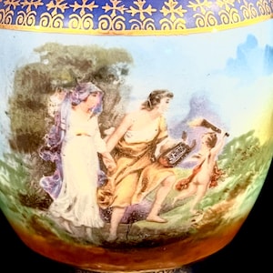 May include: A detailed image of a decorative vase with a painted scene. The scene depicts figures in classical attire, set against a backdrop of trees and sky. The vase has a blue and gold rim.