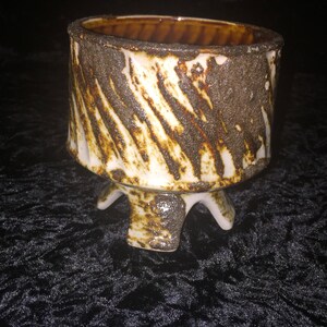 May include: A white ceramic planter with brown and black glaze. The planter has three legs and a wide, round opening.
