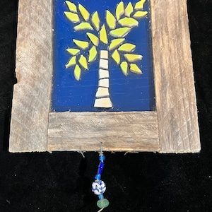 May include: A rustic, framed mosaic featuring a palm tree design. The tree has a white trunk and yellow leaves against a blue background. The frame is made of weathered wood. A beaded ornament hangs below.