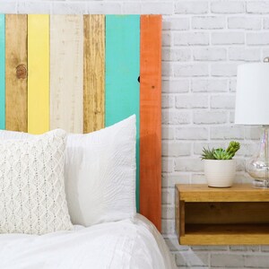 Close up view of a floating minimalist headboard queen size bed built with real wood planks, stained with a light brown colors, and painted with white, mint, apricot and yellow hues for a bohemian home decor style. Paired with a brown nightstand.