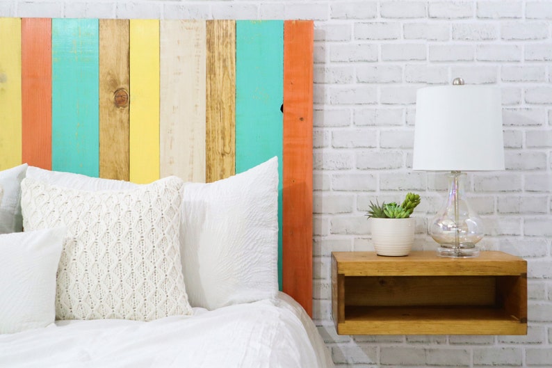 Close up view of a floating minimalist headboard queen size bed built with real wood planks, stained with a light brown colors, and painted with white, mint, apricot and yellow hues for a bohemian home decor style. Paired with a brown nightstand.