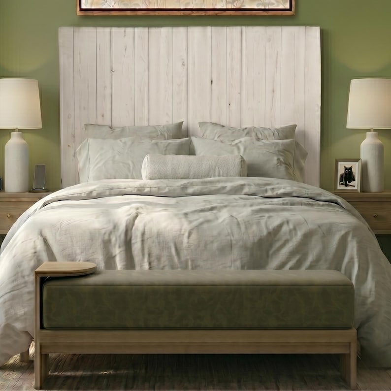 May include: A rectangular upholstered bench with a muted olive green seat and a light wood frame. The bench features a small, integrated circular side table on the left end. The piece is positioned at the foot of a bed with a white headboard.