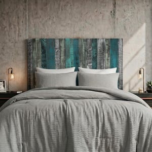May include: A rectangular headboard made of vertical wooden planks in shades of teal, dark blue, and grey. The bed is dressed in a textured light grey comforter and two matching pillows. Two metal lamps with Edison bulbs sit on side tables.
