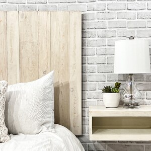 Partial view of a floating headboard queen size bed built with real wood planks painted antique white color cottage style. The headboard is weathered and distressed, paired with a minimalist antique white wood stain floating nightstand.