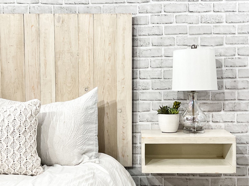 Partial view of a floating headboard queen size bed built with real wood planks painted antique white color cottage style. The headboard is weathered and distressed, paired with a minimalist antique white wood stain floating nightstand.