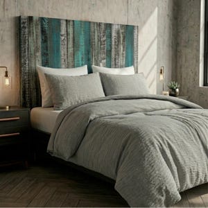 May include: A bed featuring a headboard made of vertical wooden planks in shades of teal, grey, and brown. The bed is dressed with a textured grey comforter and two matching grey pillows, complemented by two white pillows placed behind them.