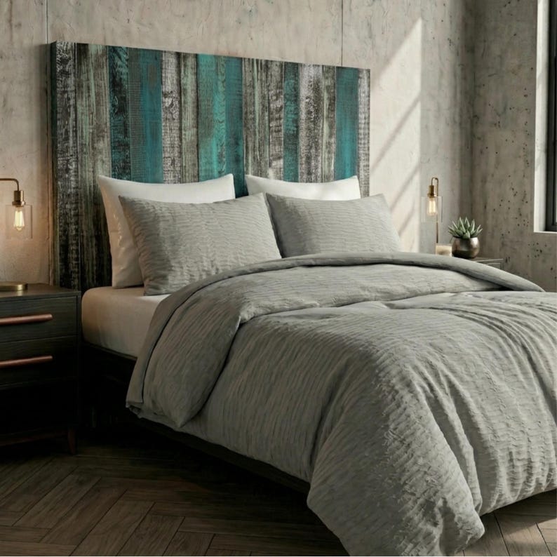 May include: A bed featuring a headboard made of vertical wooden planks in shades of teal, grey, and brown. The bed is dressed with a textured grey comforter and two matching grey pillows, complemented by two white pillows placed behind them.