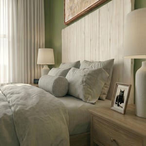 May include: A bedroom scene featuring a white vertical plank headboard against a green wall. The bed is dressed in light gray bedding with a cylindrical bolster pillow and two square pillows. Two white table lamps and a framed cat photo are present.