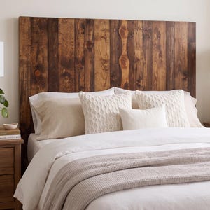 May include: A rectangular headboard constructed from vertical dark brown wooden planks with visible wood grain and knots. The headboard is positioned behind a bed featuring white bedding, a textured waffle-weave blanket, and several decorative pillows.