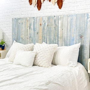 Partial view of a floating headboard queen size bed built with real wood planks stained with a blue color, washed with a white finished for a coastal cowgirl home decor style. Paired with a minimalist antique white wood stain floating nightstand.