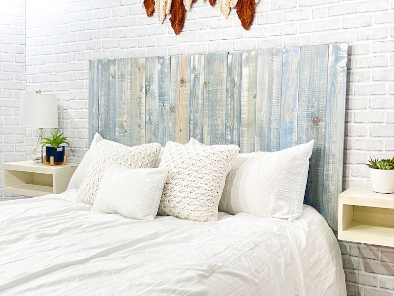 Partial view of a floating headboard queen size bed built with real wood planks stained with a blue color, washed with a white finished for a coastal cowgirl home decor style. Paired with a minimalist antique white wood stain floating nightstand.