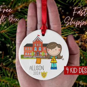 Könnte beinhalten: Runder weißer Keramik-Weihnachtsschmuck mit rotem Band. Er zeigt eine Cartoon-Illustration eines Schulgebäudes und eines Mädchens mit einer Fahne. Der Schmuck ist mit dem Namen "ALLISON" und dem Jahr "2024" personalisiert.