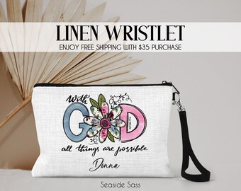 May include: White linen wristlet with a black zipper and a black wrist strap. The wristlet has a floral design with the words "With God all things are possible Donna" printed on it.