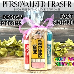 May include: A personalized eraser gift set featuring a wooden pencil-shaped eraser with "MRS. BINFORD" printed on it, accompanied by two Expo dry-erase markers. The set is wrapped in clear cellophane and tied with a pink ribbon. The text "16 DESIGN OPTIONS" is also visible.