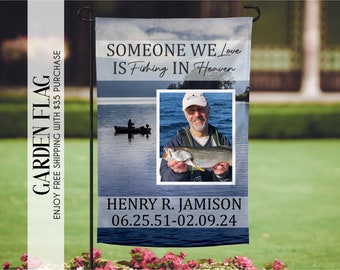 May include: A blue and white garden flag with a photo of a man holding a fish. The text on the flag reads "Someone we love is fishing in heaven" and "Henry R. Jamison 06.25.51-02.09.24".