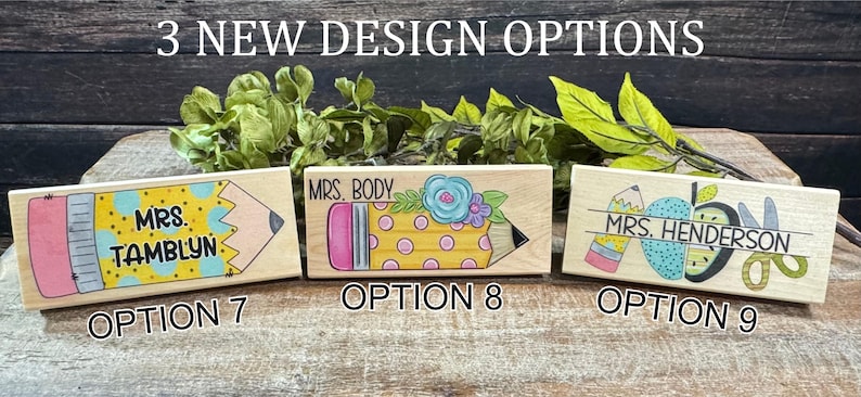 May include: Three wooden teacher desk nameplates with pencil and apple designs. Each nameplate features a different design and name, with options 7, 8, and 9 labeled below. The nameplates are painted with bright colors and are displayed on a wooden surface.