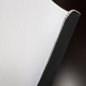 May include: A rectangular mouse pad featuring a smooth, light gray surface and a contrasting black underside. The edges are reinforced with a white stitched border that provides a clean finish to the durable, functional computer accessory.