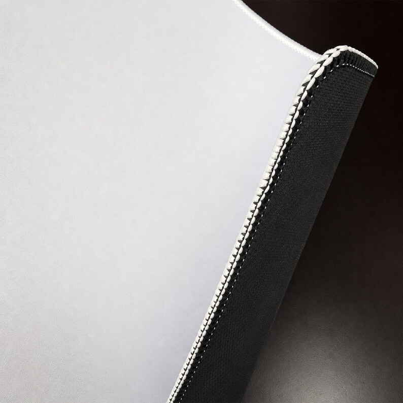 May include: A rectangular mouse pad featuring a smooth, light gray surface and a contrasting black underside. The edges are reinforced with a white stitched border that provides a clean finish to the durable, functional computer accessory.